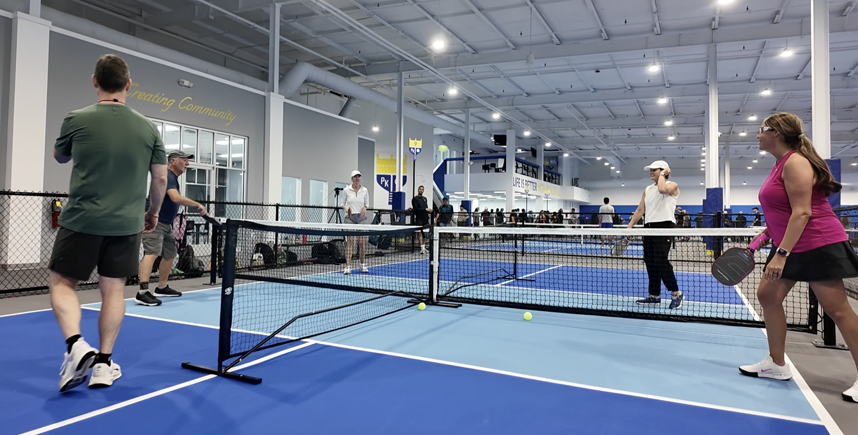 Players rallying across a net on an indoor pickleball court